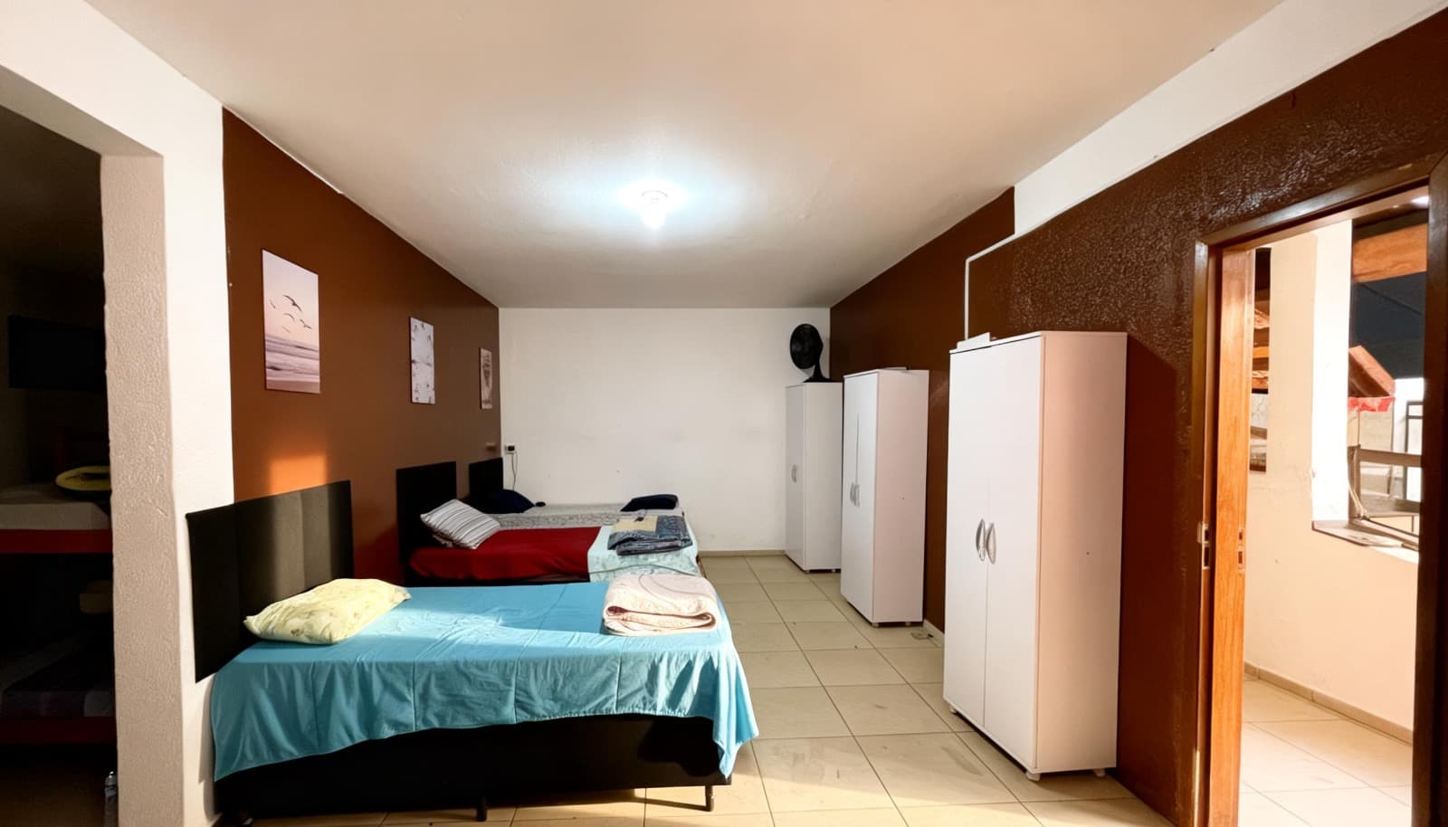 Quarto com três camas, roupas de cama e armários individuais.