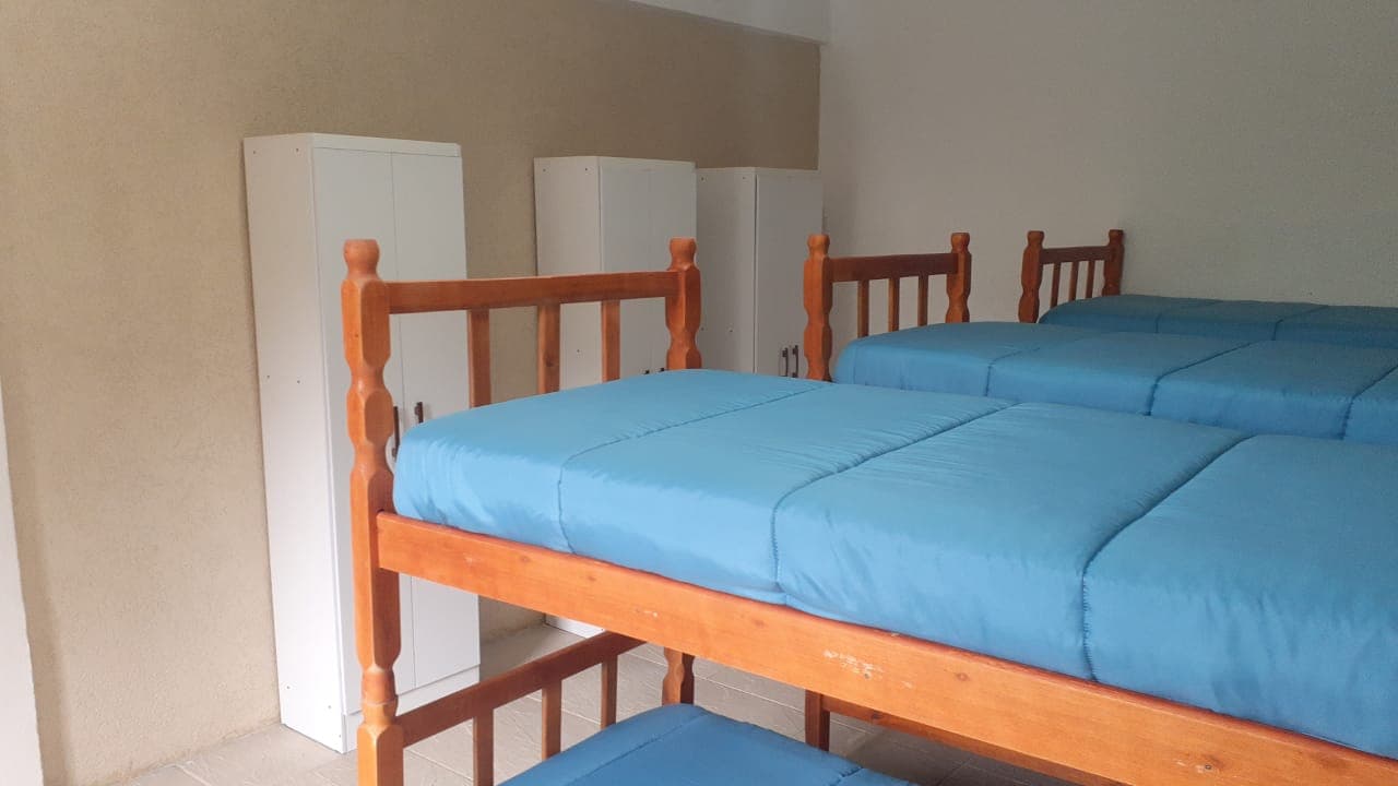 Quarto com beliches, roupas de cama azuis e armários individuais.
