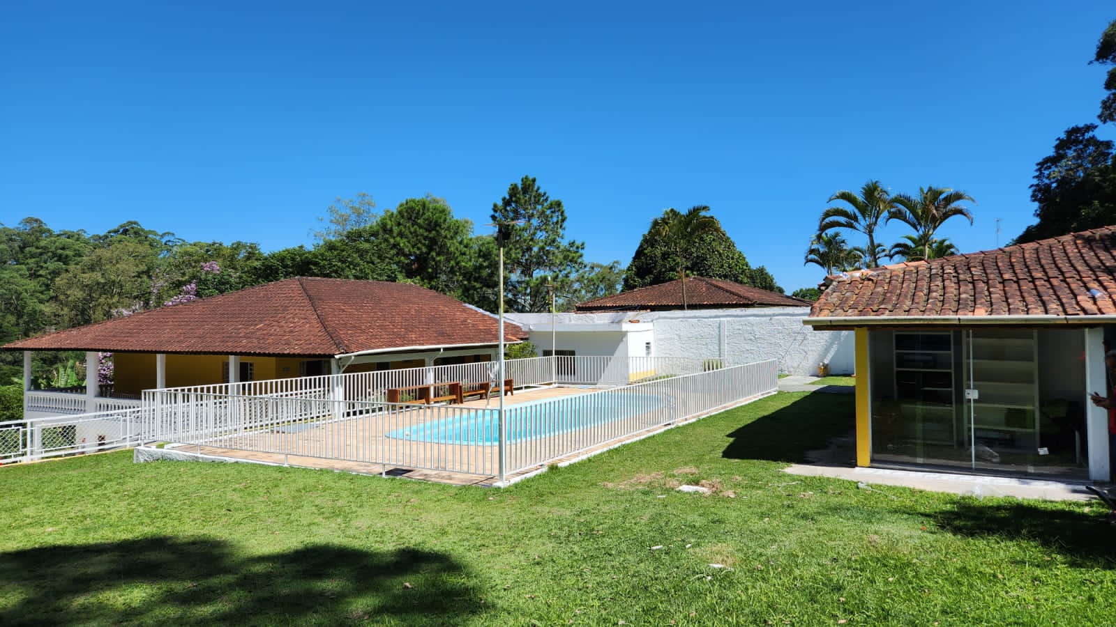 Área externa da Arhat com piscina cercada, gramado e construções.
