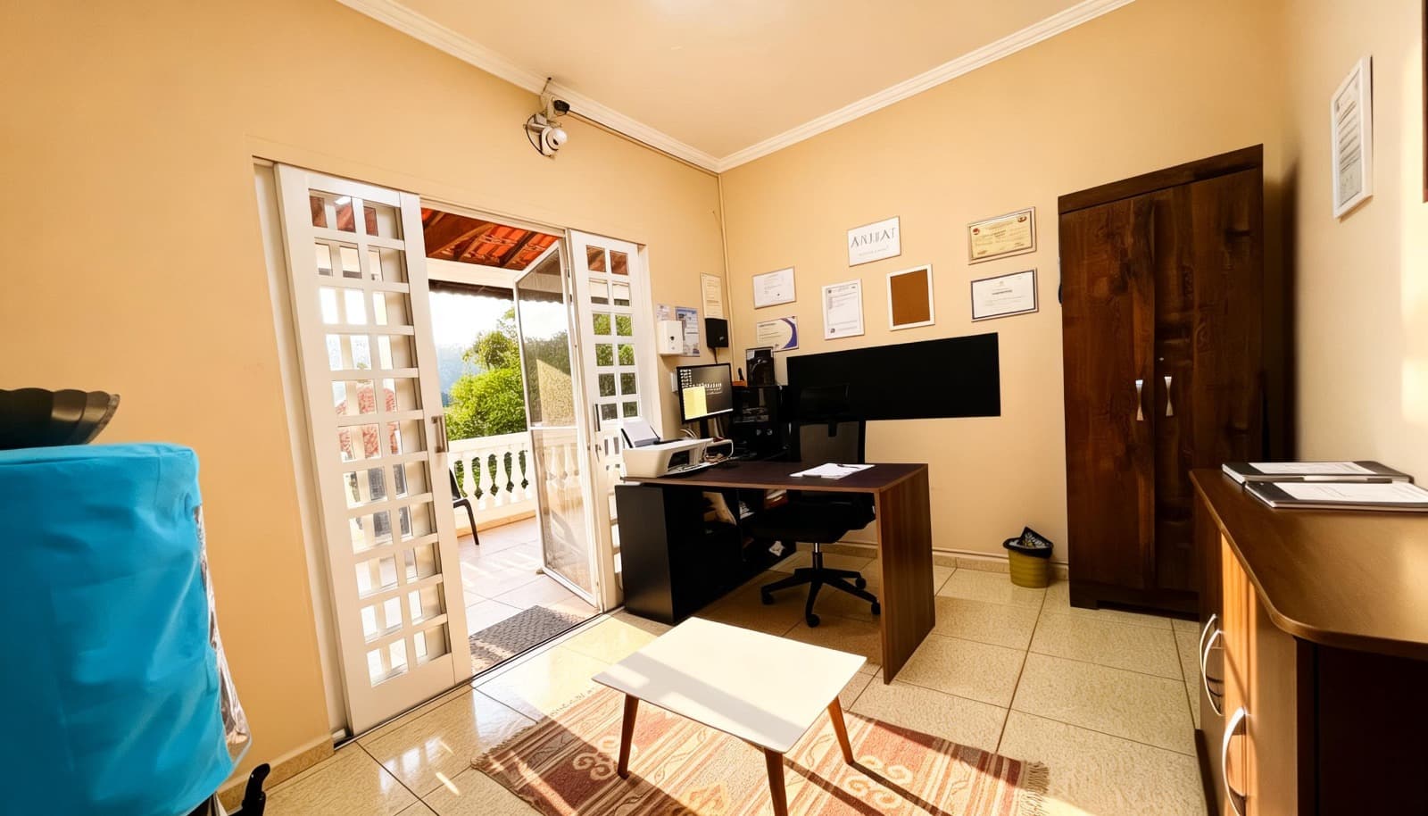 Sala de recepção e escritório com mesa, computadores e acesso à varanda.