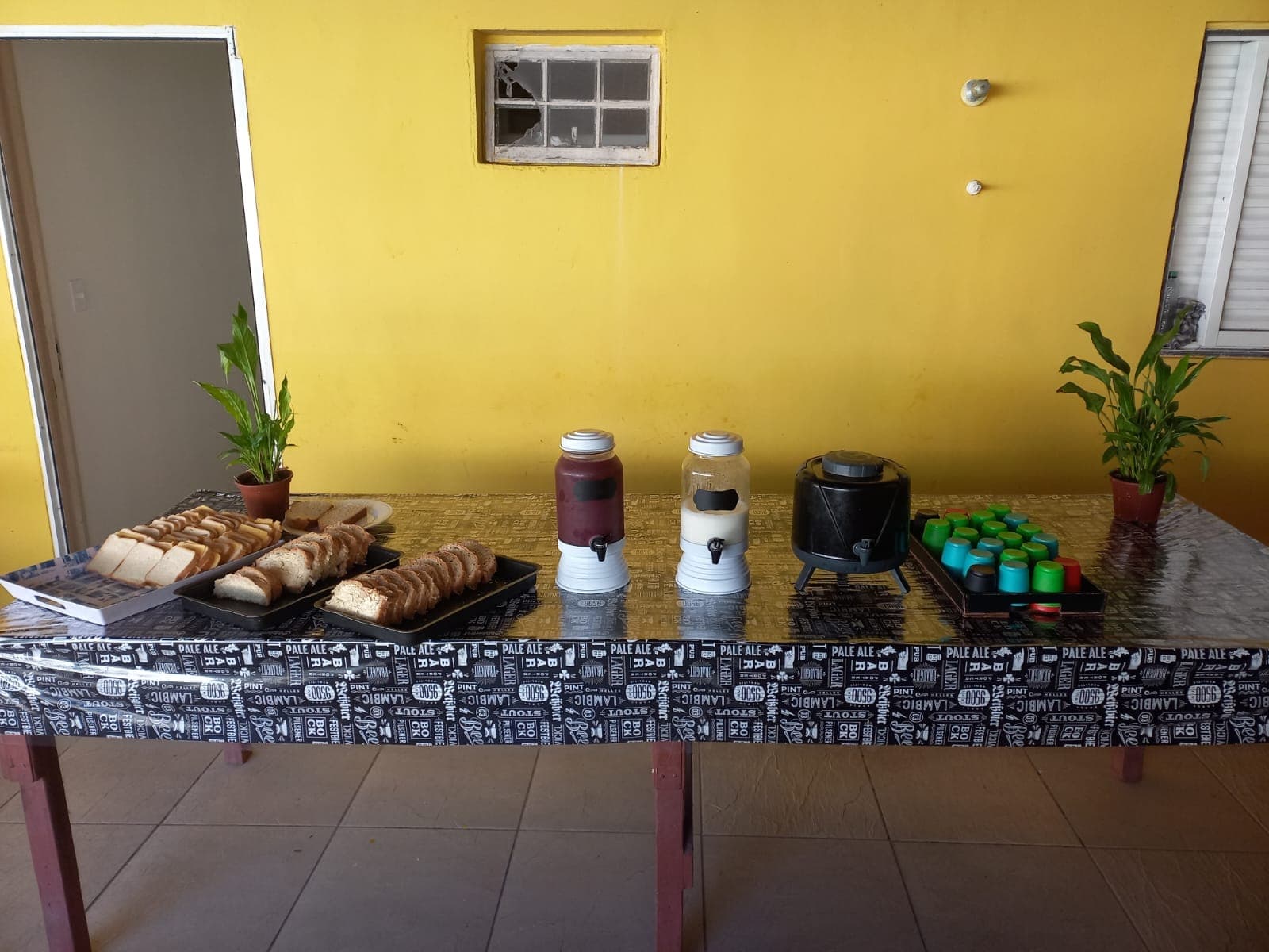 Mesa de café com pães, bebidas e utensílios organizados.