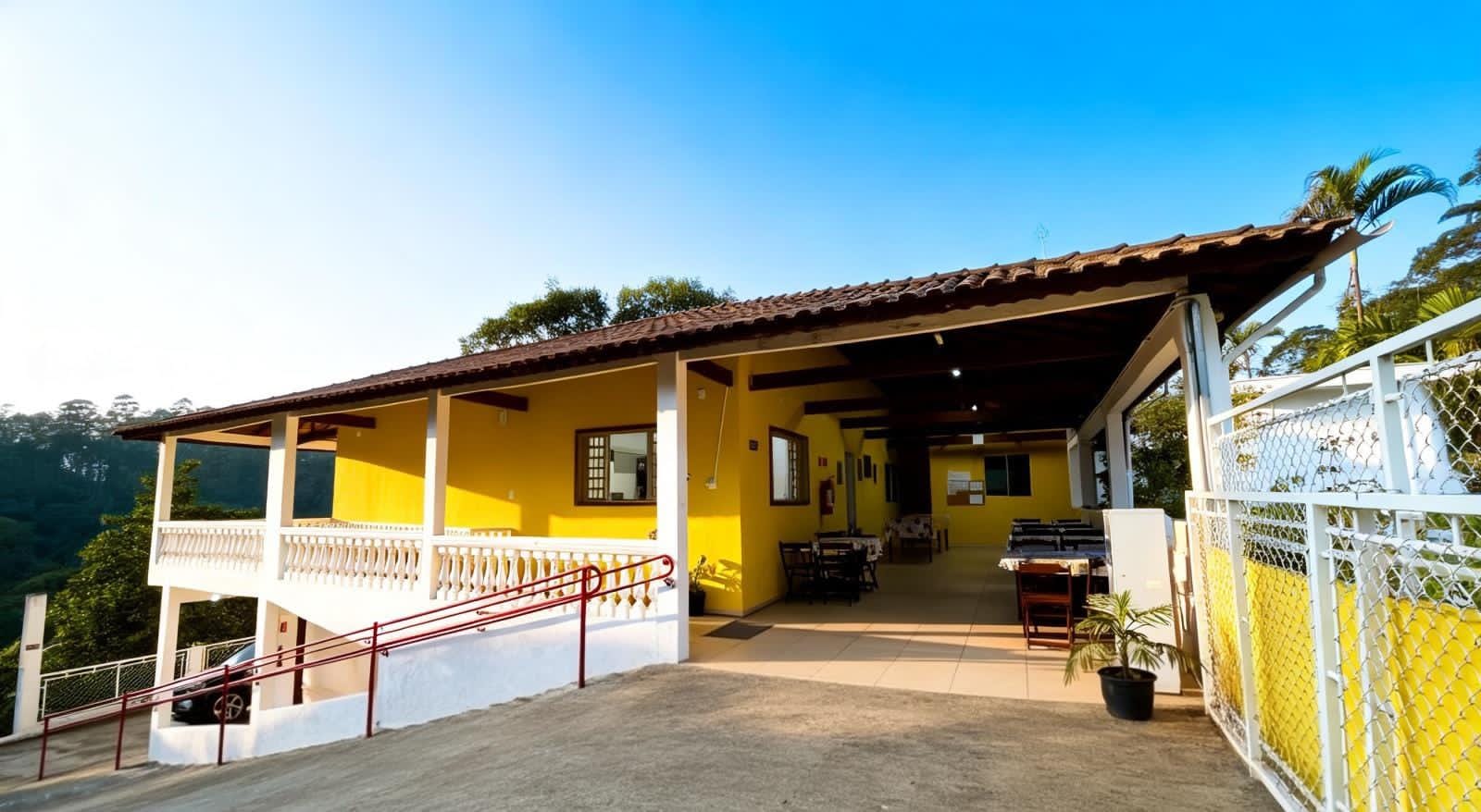 Fachada amarela da Arhat com varanda coberta, rampa e portão.