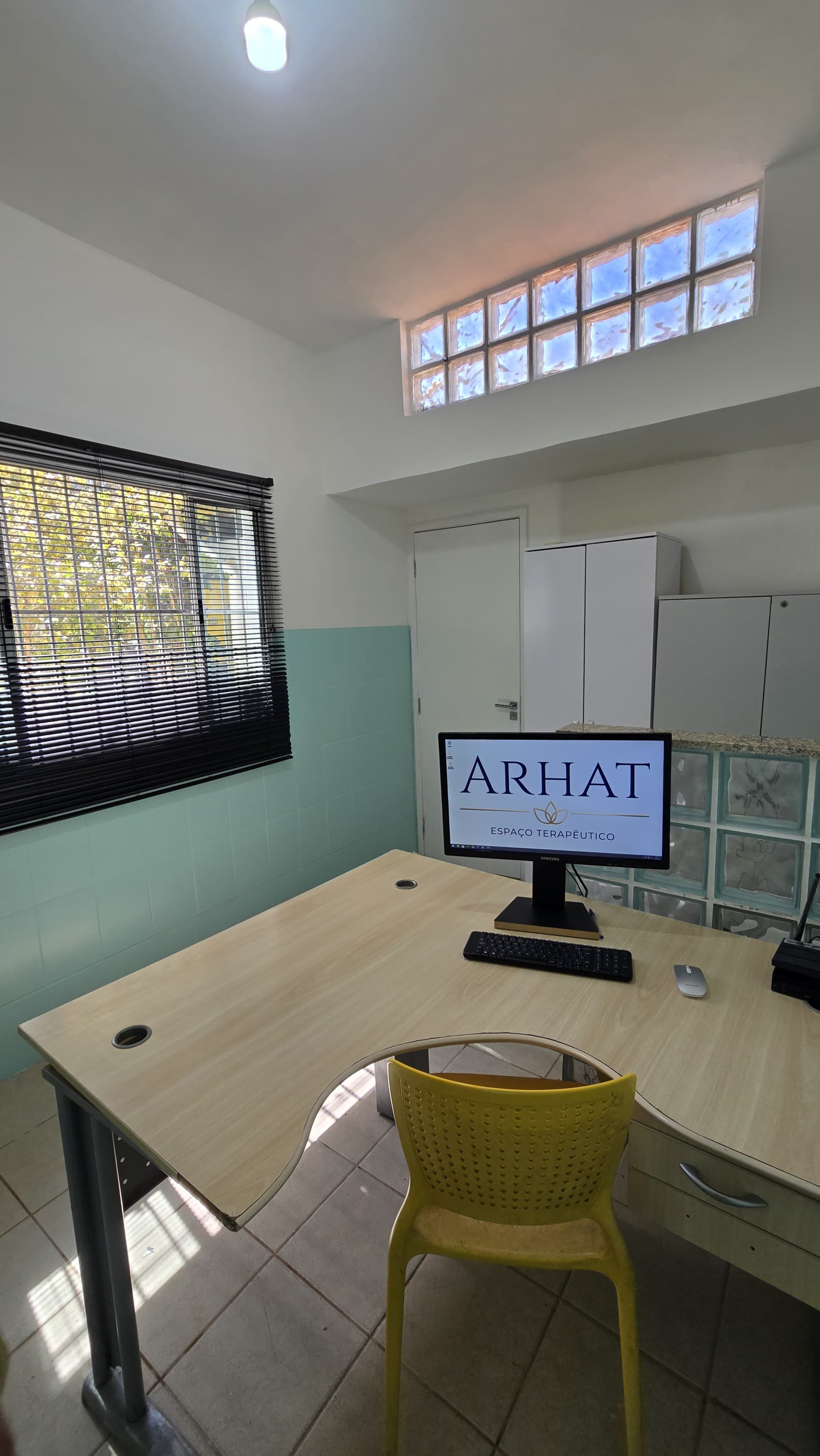 Enfermaria da Arhat com mesa, computador, armários e divisória de blocos de vidro.