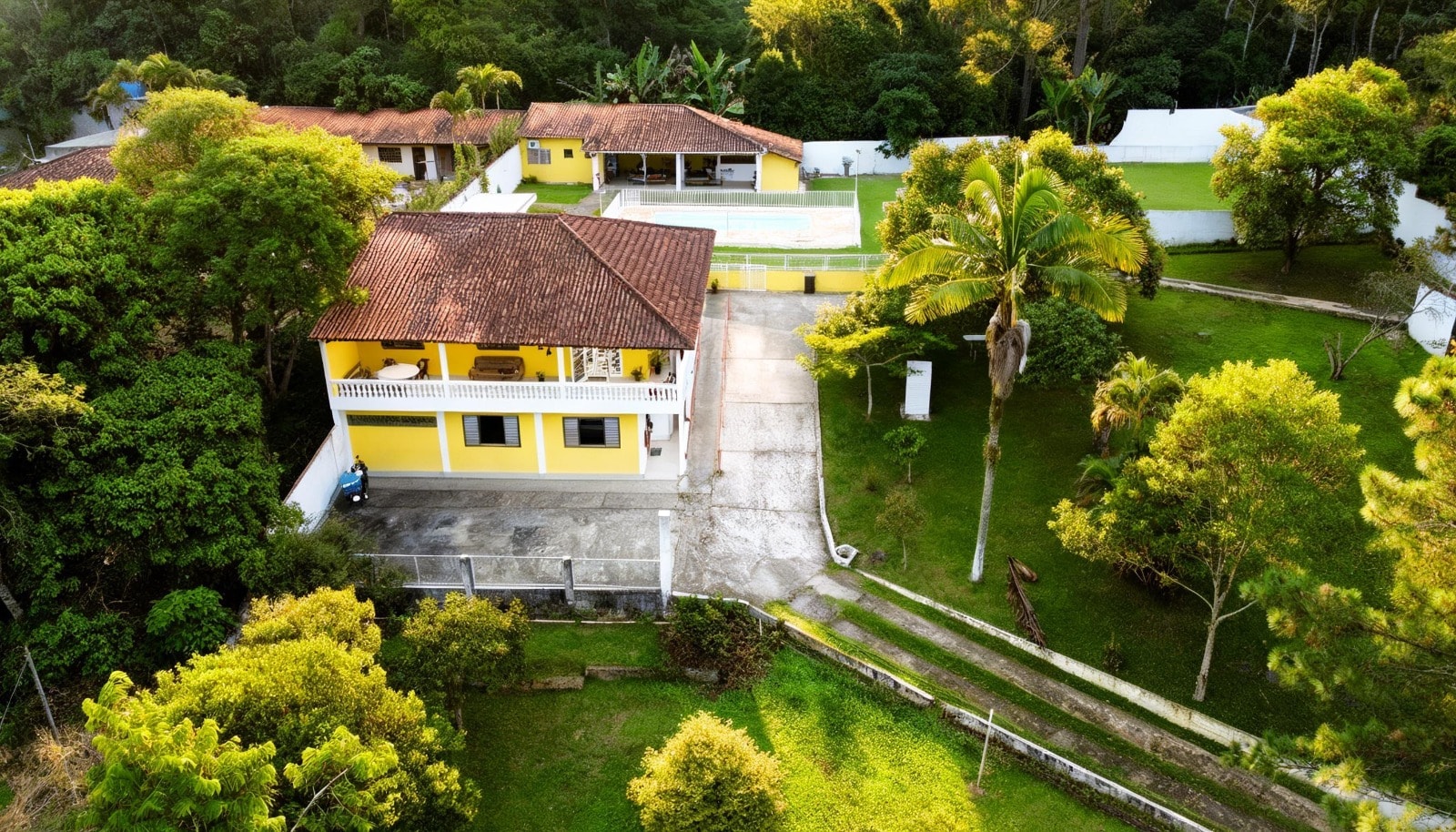 Vista aérea da propriedade Arhat, com residência, piscina e área verde cercada por árvores.